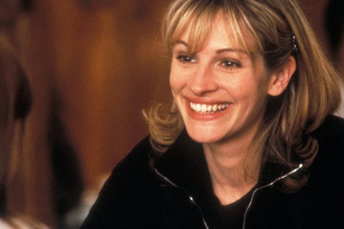 A person smiles broadly, looking engaged in conversation, set against a warm, softly focused background.