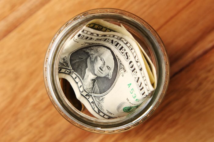 A savings jar filled with american dollars on a wooden table top.
