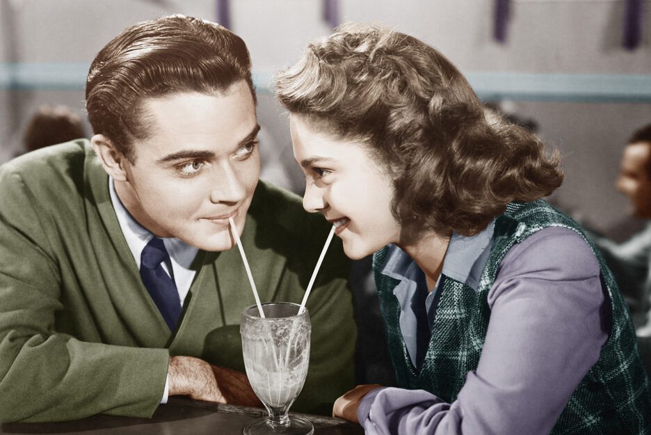 Couple in a restaurant looking at each other and sharing a milk shake with two straws