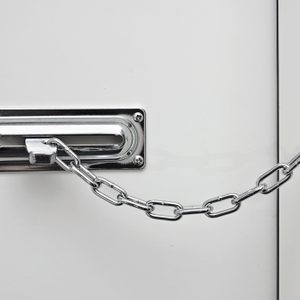 Chain lock secures door, connecting mounted plates; one rectangular, the other square, against a white background.