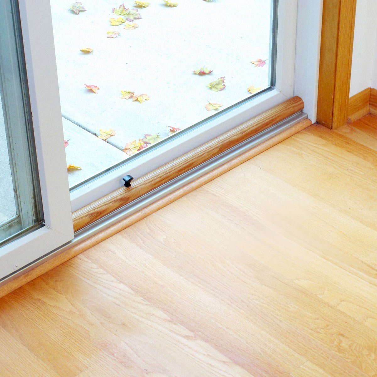Sliding glass door partially open, revealing autumn leaves scattered on outdoor patio, with wooden flooring inside.