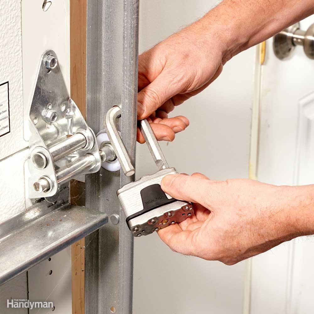Hands locking a padlock onto a garage door track, securing it. The context is a close-up of the mechanism and door hardware.