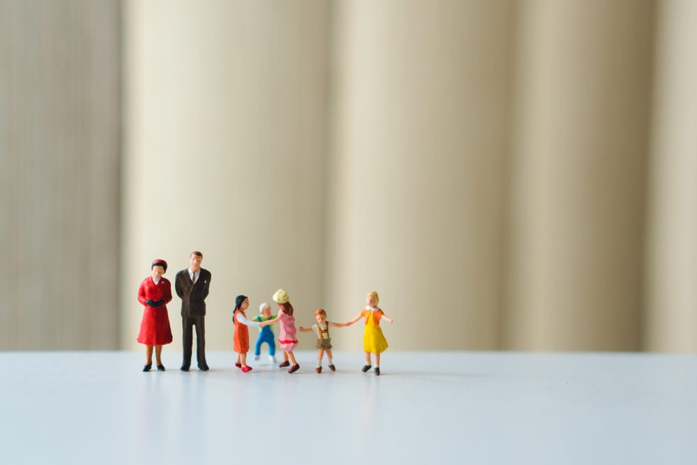 Miniature figures stand together, interacting on a smooth surface; blurred vertical background provides a neutral setting for the tiny group.