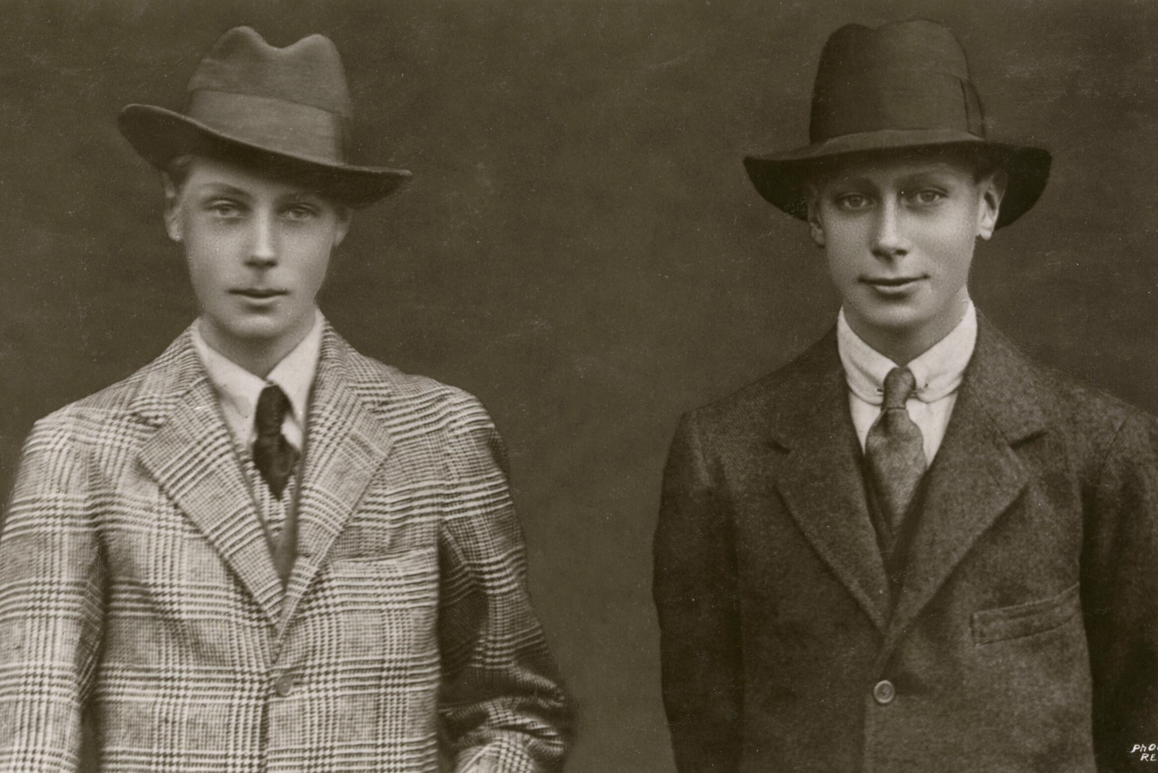 Two young men pose wearing suits and hats, standing against a plain background. The text reads "Photo Reveley."