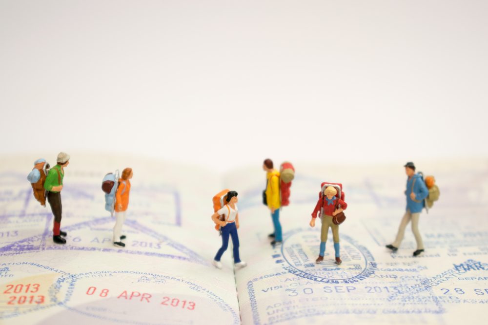 Miniature figures hike across passport pages stamped with travel dates.