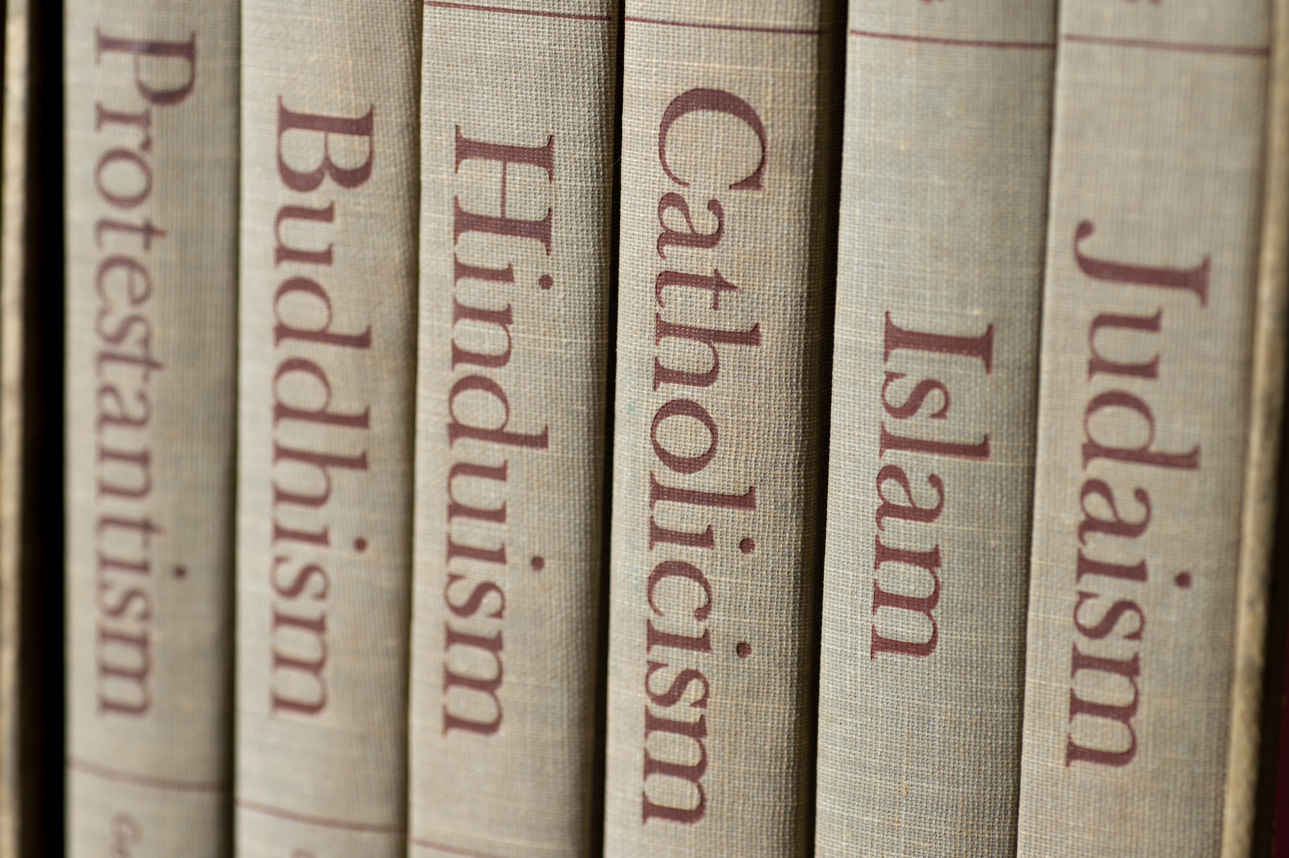 Book spines listing major world religions - Judaism, Islam, Catholicism, Hinduism, Buddhism and Protestantism. The focus is on the word, Catholicism.