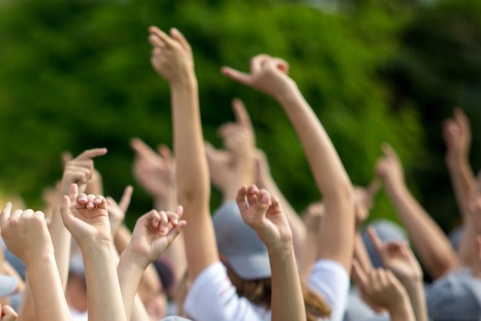 Group of happy young people with hands up to the sky over green natural background