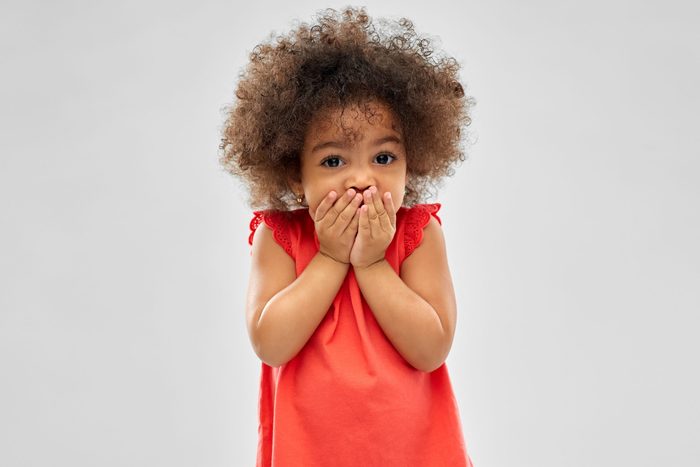 childhood, expression and emotion concept - confused little african american girl covering mouth by hands over grey background
