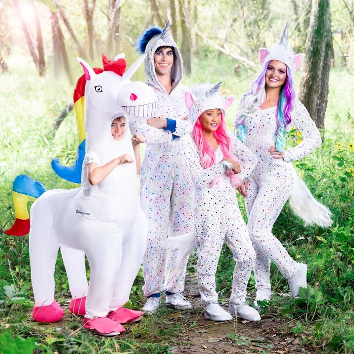 People wearing unicorn costumes pose in a sunlit forest clearing, surrounded by lush greenery.