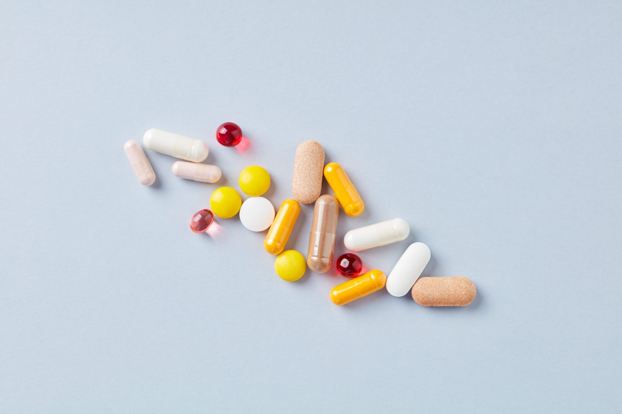 Multicolor vitamins and supplements on bright paper background. Concept for a healthy dietary supplementation. Top view. Copy space. 