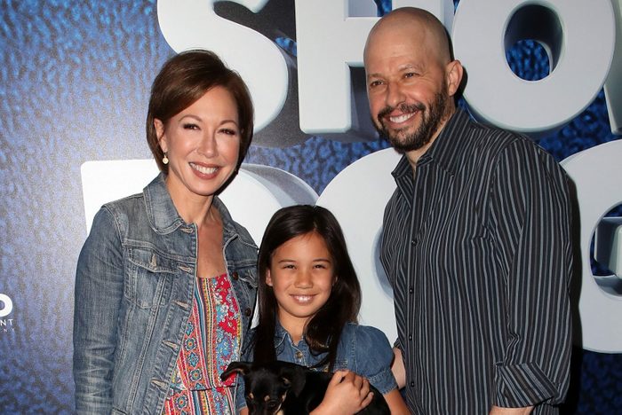 A girl holds a small dog, standing with two adults. They smile on a blue carpet in front of a promotional backdrop.