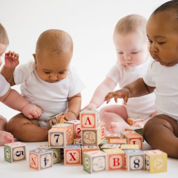 Babies sit and explore colorful alphabet blocks on a bright, clean white background.