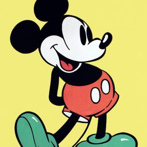 Character stands smiling with one leg forward, hands behind back, against a plain yellow background.