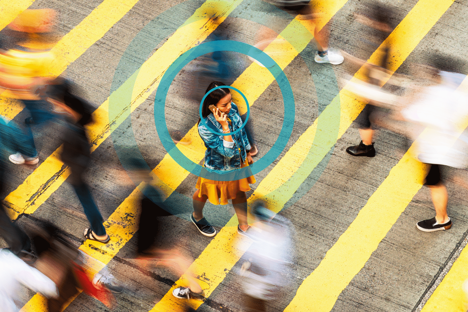 Person talks on phone, standing amidst moving crowd on yellow-striped crosswalk, with overlapping blue circles emphasizing focus.
