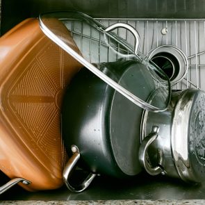 Pots and a glass lid stack in a stainless steel sink, draining water, on a granite countertop background.