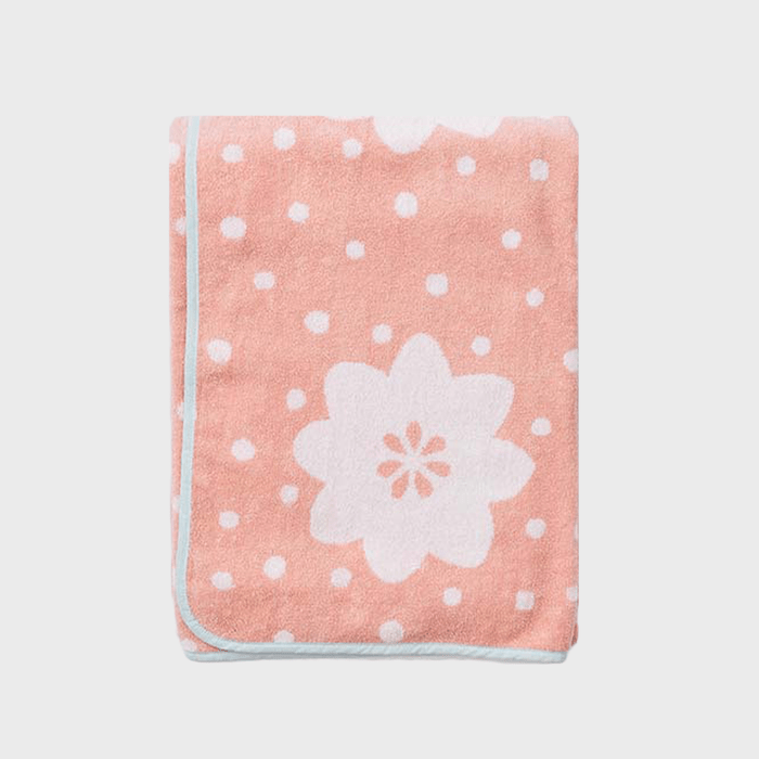 A pink folded blanket features white flower and polka dot patterns, with a light blue border, set against a plain background.