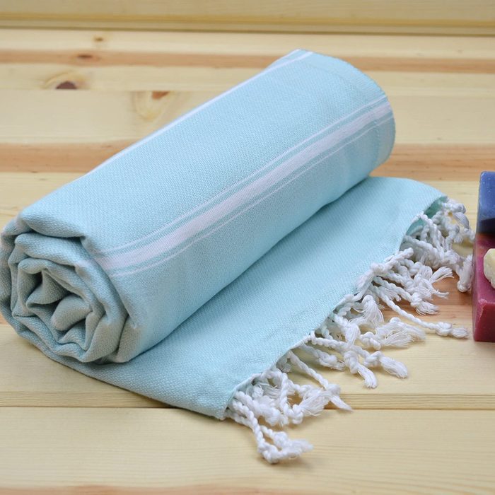 A rolled, light blue towel with white tassels rests on a wooden surface.