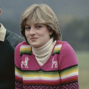 A person smiles slightly, wearing a colorful knitted sweater with llama patterns, set against a blurred outdoor background.
