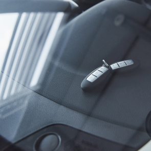 A car key sits on a dark dashboard, viewed through a windshield, with reflections of vertical lines.