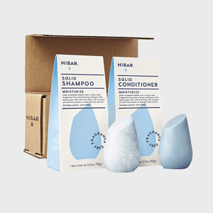 Solid shampoo and conditioner stand upright; each with blue packaging and descriptive text, including 