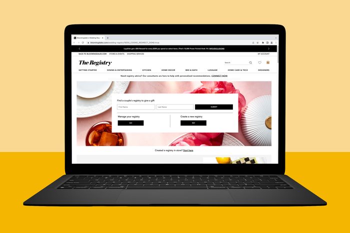 Laptop displays wedding registry webpage; options include finding, managing, or creating a registry, with floral tableware background; seen against a yellow backdrop.