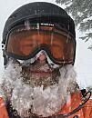 Person wearing ski goggles and helmet, face covered in snow, standing in a snowy outdoor environment.