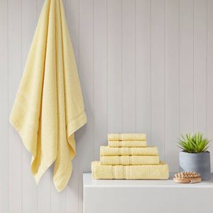 Yellow towel hangs, others neatly stacked beside a potted plant and brush, against a light wood-paneled wall.