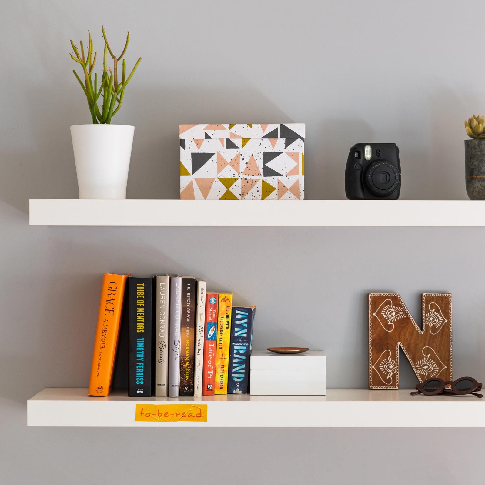 two modern and minimalist bookshelves on the wall with decoration and a small section with books labeled "to-be-read"