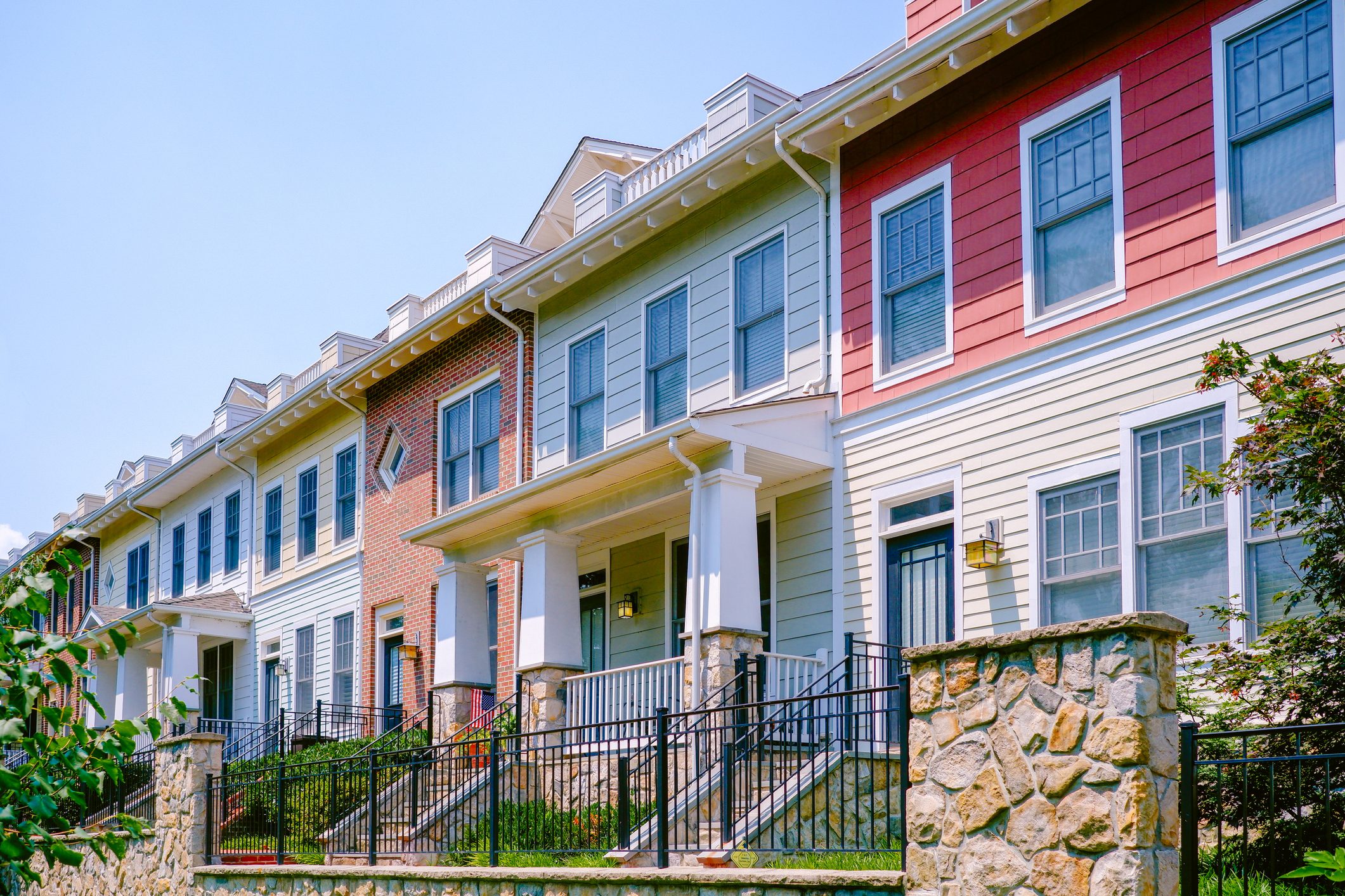 Row of colorful townhouses stand with stone fences under a clear blue sky.