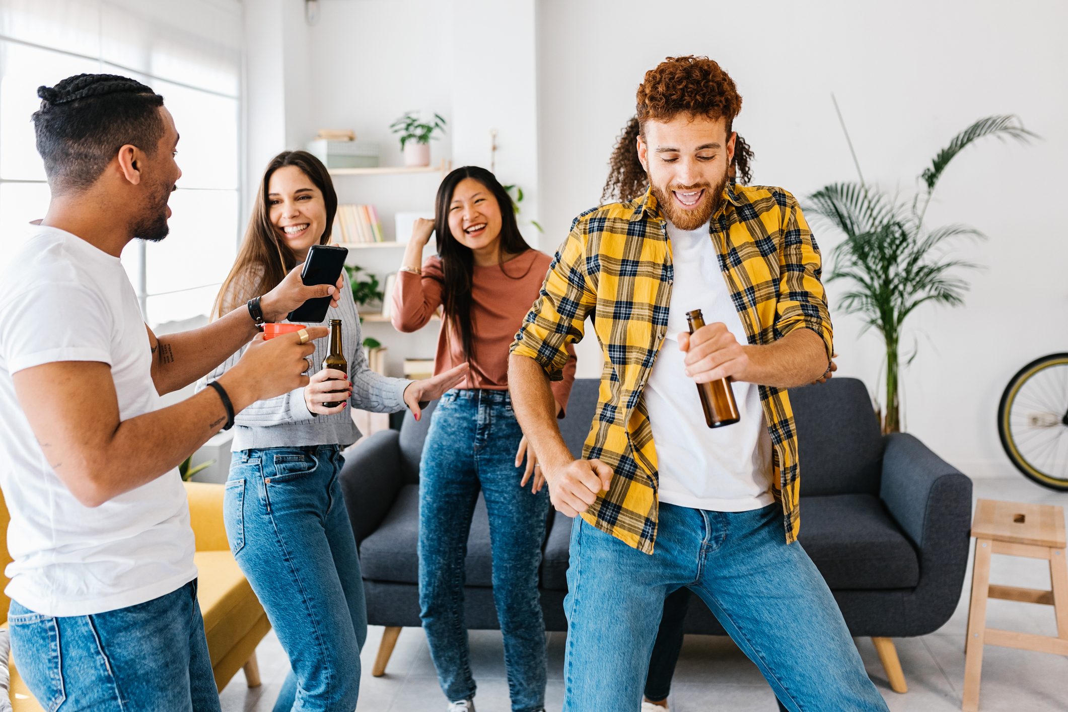 Multi ethnic group of young student friends dancing and celebrating together while having party at home