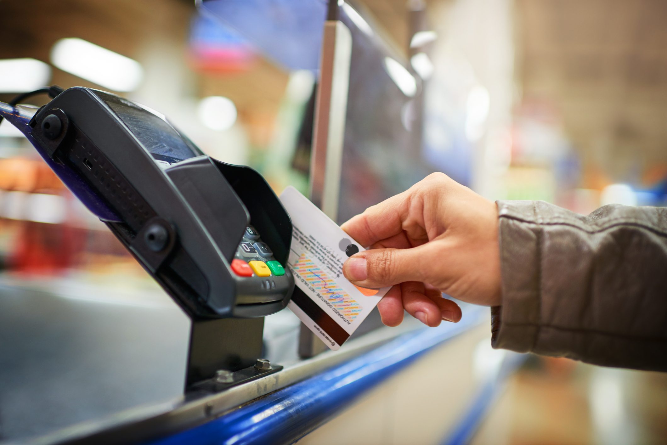 A credit card is being inserted into a payment terminal on a shop counter.