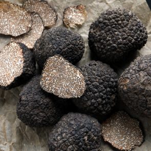 Whole and sliced black truffles rest on crumpled parchment paper, showing their textured, dark exteriors and intricately veined interiors.
