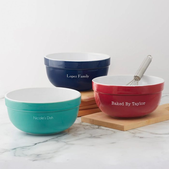 Three ceramic bowls sit on counter; one red with whisk, one teal, and one blue, each labeled with names.