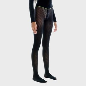 Person wearing patterned black tights stands against a plain light background, with arms relaxed by their sides.