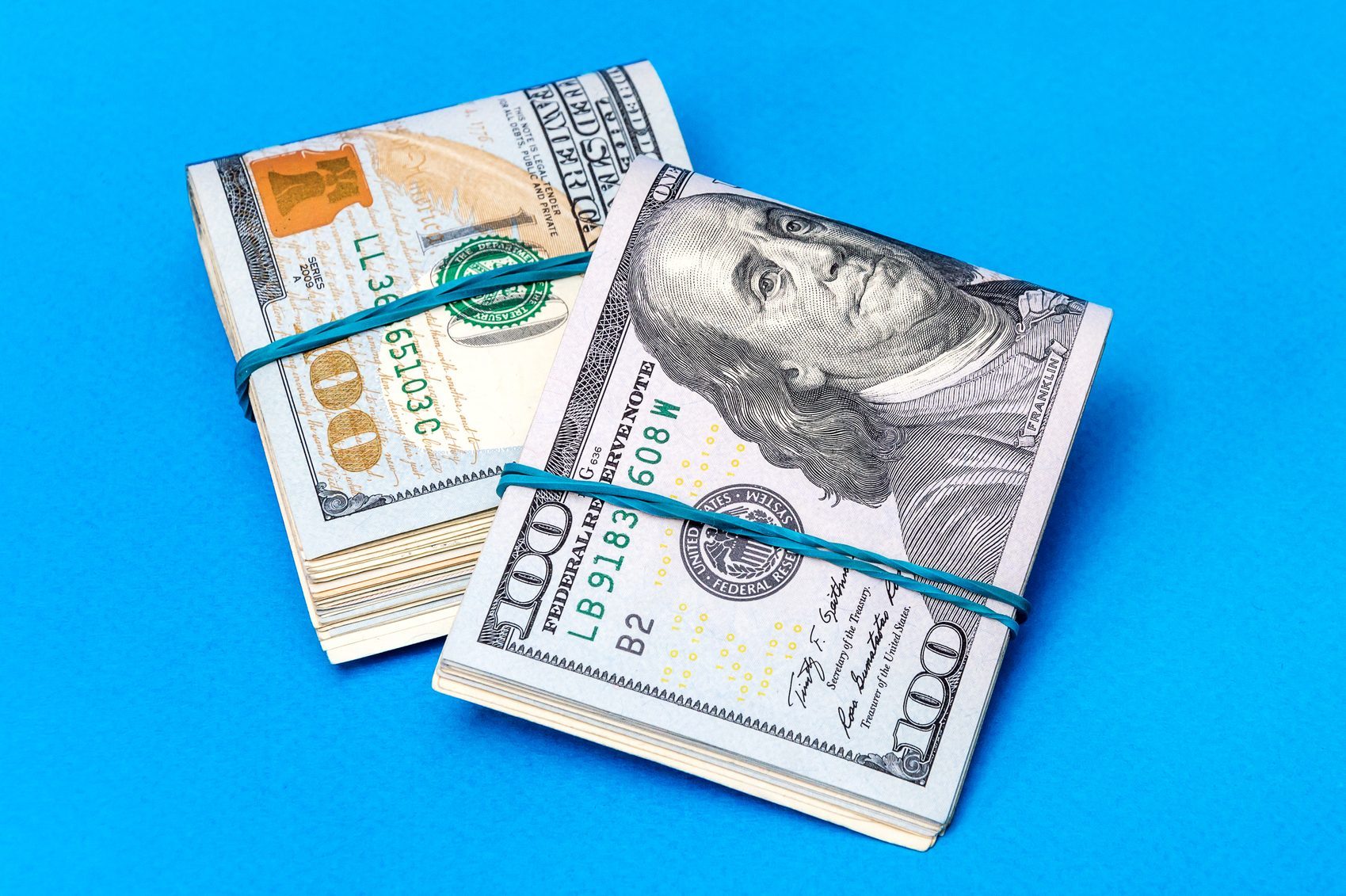 Stacks of US 100-dollar bills secured with rubber bands on a blue background.