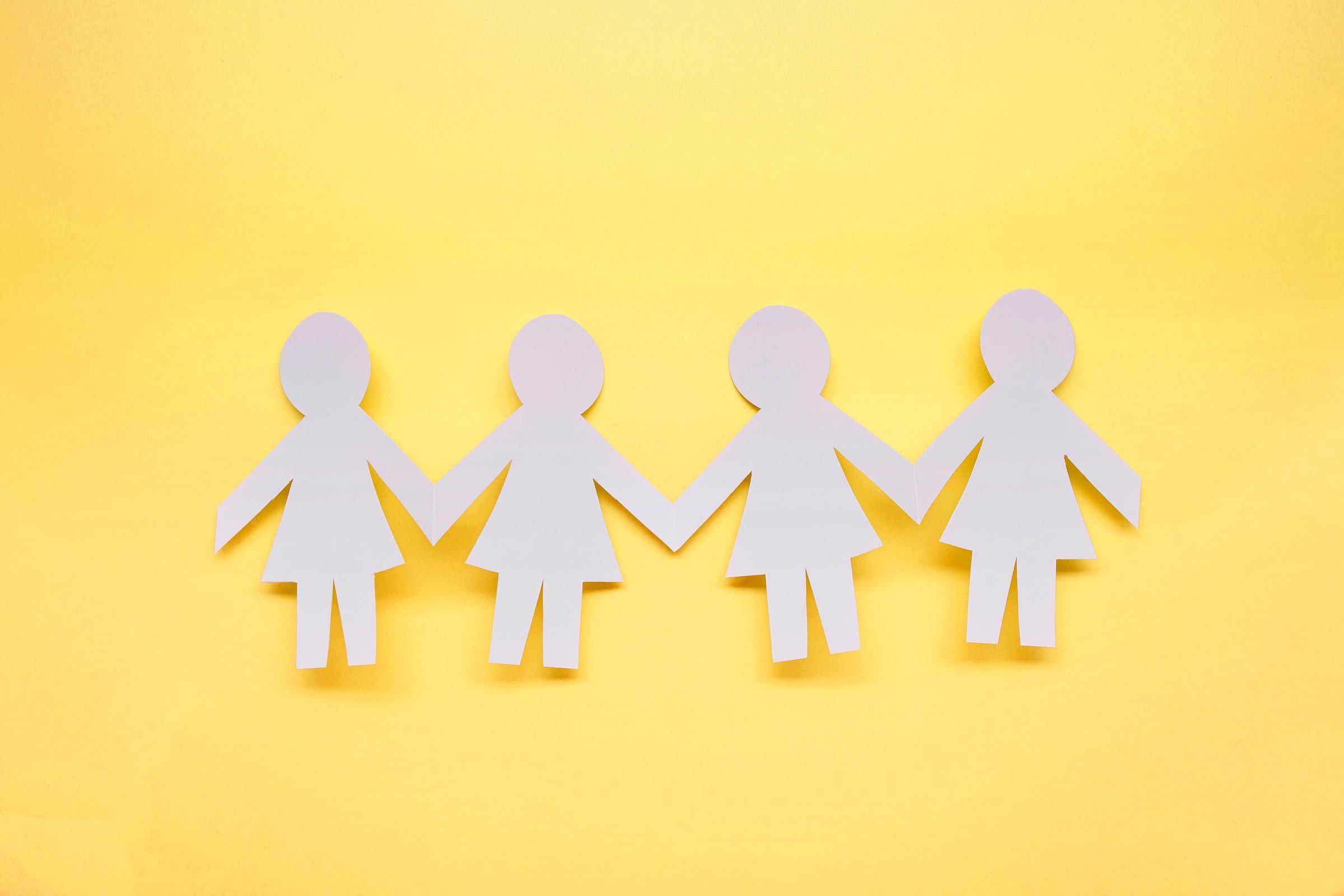 Four white paper dolls holding hands against a bright yellow background.