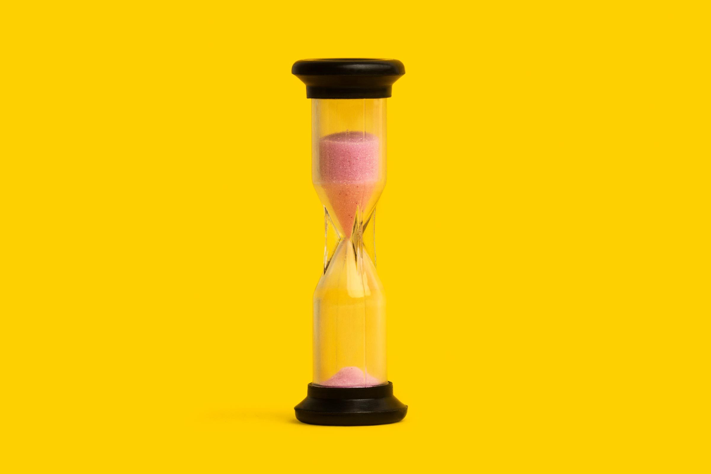 Hourglass with pink sand falls through a narrow center, set against a vibrant yellow background.