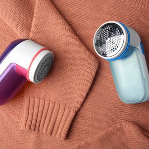 Two fabric shavers resting on a peach-colored knit sweater, with one shaver featuring purple accents, and the other with blue.