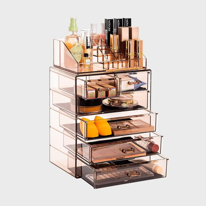 Organizer holds assorted cosmetics in transparent compartments, including sprays, lipsticks, and powders, neatly arranged against a plain background.