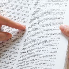 Finger points to dictionary page with definitions, focusing on the word 