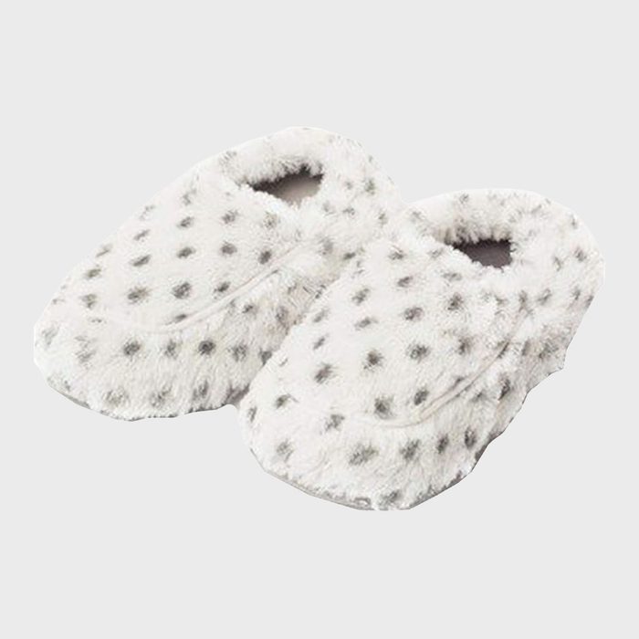 Fuzzy white slippers are lying together with gray polka dots, against a plain gray background.