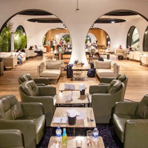 Chairs surround tables with drinks, while people relax and converse in a spacious lounge with circular openings and modern decor.