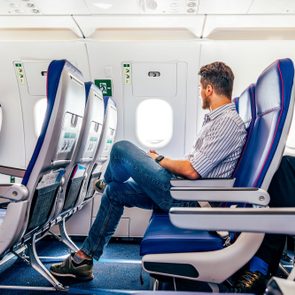 A person sits, looking out an airplane window, in a row of empty blue seats with safety instruction cards visible.
