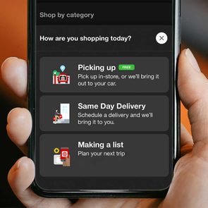Hand holding phone displaying shopping options: Picking up, Same Day Delivery, Making a List, with icons and descriptions against a blurred background.
