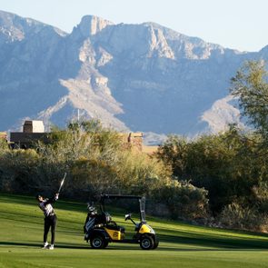 Person golfing next to a golf cart in the late afternoon, with mountains in the background