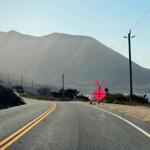 A pink road sign with two flags sticking out of it saying 