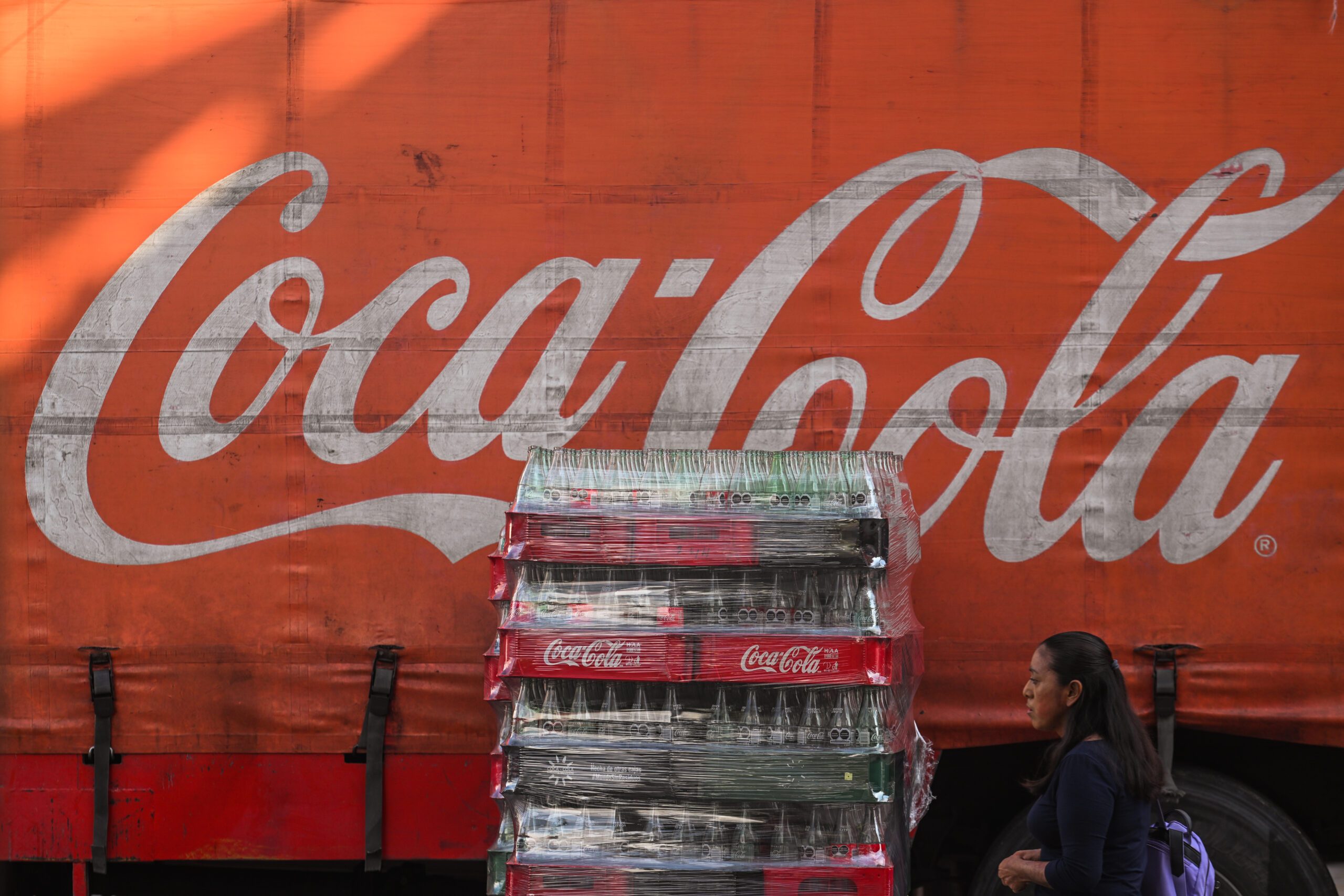 Cases of coca cola bottles in front of a red Coca Cola mural