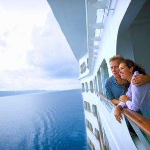 Couple leaning on rail of cruise ship, looking at ocean