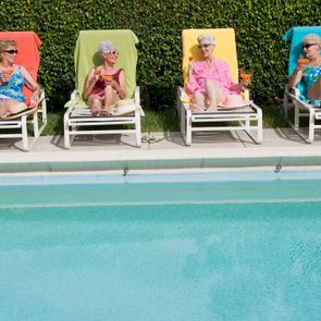 Four women on multicolored towels and pool lounge chairs next to a pool