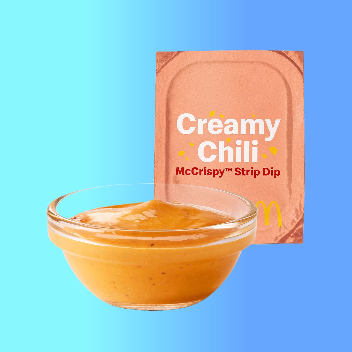 Pink McDonald's creamy chili sauce packet with a bowl of the sauce on a blue background